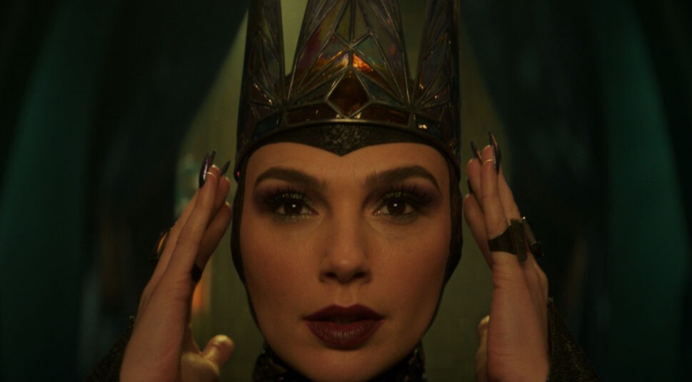 Auf dem Bild zur Schneewittchen Realverfilmung ist Gal Gadot als Böse Königin zu sehen. Sie trägt eine gläsern wirkende, spitz zulaufende Krone und dunkles Make-up mit betonten Lippen. Ihre Hände halten die Krone, während ihr Blick intensiv in die Kamera gerichtet