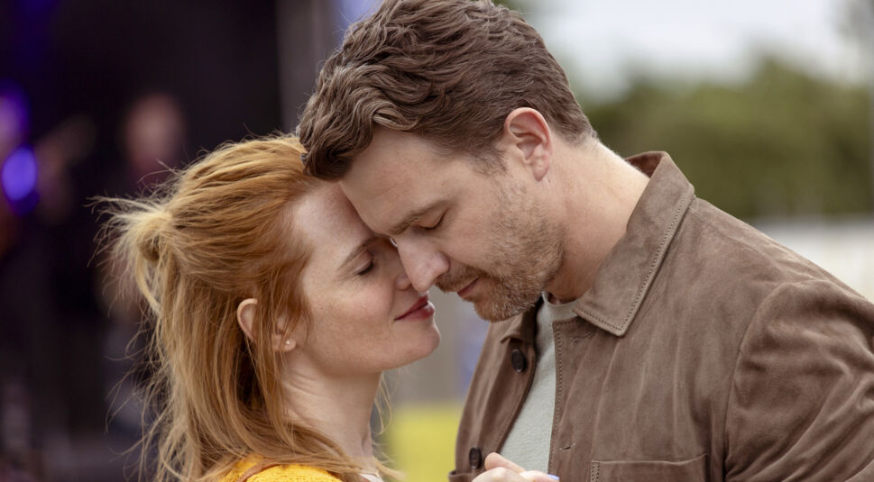 Auf dem Bild aus dem Film Wunderschön mit Karoline Herfurth sind Sonja (Karoline Herfurth) und Milan (Friedrich Mücke) in einer innigen und romantischen Szene zu sehen. Sie stehen nah beieinander, ihre Stirnen berühren sich zärtlich, während sie die Augen schließen. Sonja trägt ein gelbes Oberteil, Milan eine braune Wildlederjacke. Die Stimmung ist liebevoll und warm.