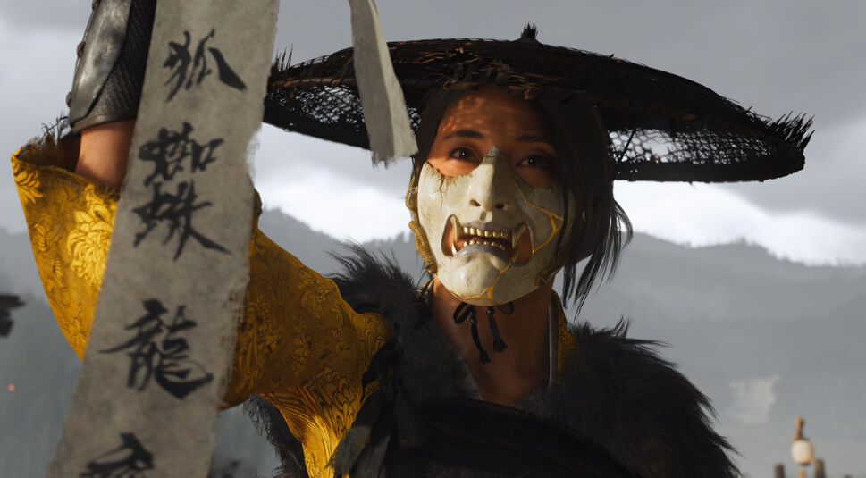 Auf diesem Bild aus dem Spiel Ghost of Yotei ist eine Charakterin in einem auffälligen gelben Gewand mit floralen Mustern zu sehen. Sie trägt eine Maske und einen Strohhut. In ihrer Hand hält sie ein Schriftband mit Schriftzeichen.