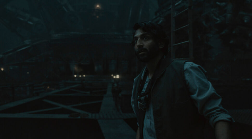 Im Silo Staffel 2 Ende erklärt-Artikel ist Avi Nash als Lukas in einer düsteren, weitläufigen Umgebung zu sehen.