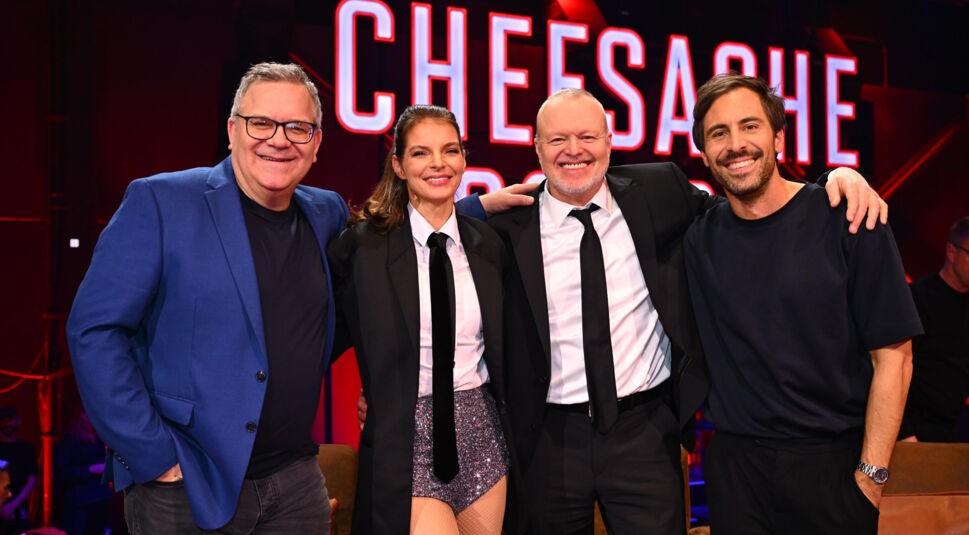 Auf dem Bild zu den GigaTV Highlights im März stehen Elton, Yvonne Catterfeld, Stefan Raab und Max Giesinger gemeinsam auf der Bühne der Show „Chefsache ESC“. Sie lachen und haben die Arme freundschaftlich umeinander gelegt. Im Hintergrund leuchtet der Show-Titel in roten Buchstaben. Die Stimmung ist ausgelassen und unterhaltsam, passend zum TV-Format.