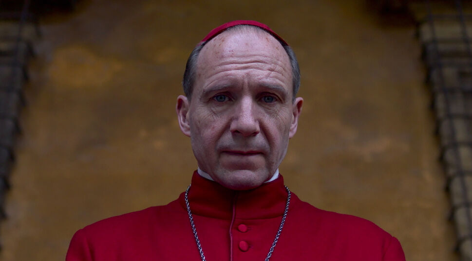 Auf dem Bild zu den GigaTV Highlights im März ist Ralph Fiennes in seiner Rolle in Konklave zu sehen. Er trägt eine rote Kardinalsrobe mit passender Kappe und eine silberne Kette. Sein Gesichtsausdruck ist ernst und nachdenklich, während der unscharfe, gold-braune Hintergrund eine feierliche Atmosphäre erzeugt. Die Szene vermittelt eine angespannte und bedeutungsvolle Stimmung.