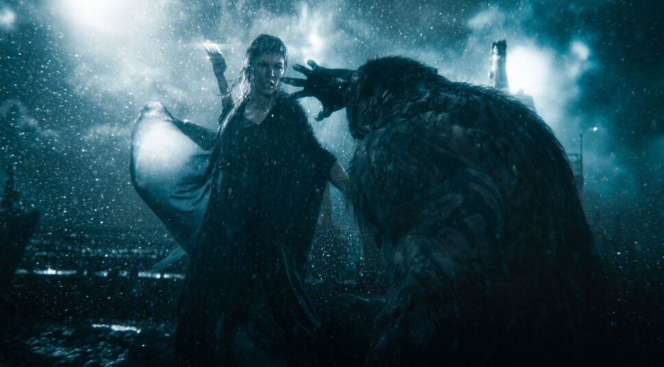 In the Lost Lands Review zeigt eine dramatische Szene, in der Gray Alys, gespielt von Milla Jovovich, einem bedrohlichen Werwolf gegenübersteht. Im strömenden Regen erhebt sie entschlossen die Hand, während das massive, fellbedeckte Wesen aggressiv reagiert.