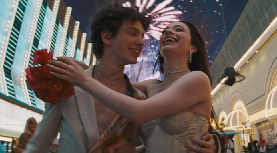 Auf dem Bild in dem Artikel zu den Oscar Filmen 2025, die bei GigaTV verfügbar sind, ist eine Szene aus dem Film Anora zu sehen. Zwei junge Menschen umarmen sich strahlend in einer lebhaften Straßenkulisse mit leuchtenden Lichtern. Der junge Mann trägt einen offenen Anzug mit Blumen, während die Frau in einem cremefarbenen Korsettkleid lacht. Im Hintergrund erhellt Feuerwerk den Nachthimmel, was die romantische und ausgelassene Stimmung der Szene unterstreicht.