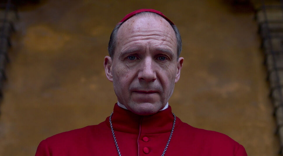 Auf dem Bild in dem Artikel zu den Oscar Filmen 2025, die bei GigaTV verfügbar sind, ist eine Szene aus Konklave zu sehen. Ein älterer Mann mit ernstem Ausdruck trägt eine rote Robe und eine Kette, während er direkt in die Kamera blickt. Sein Gesicht wirkt nachdenklich und leicht angespannt. Der Hintergrund ist unscharf, mit warmen Brauntönen, was die feierliche und ernste Atmosphäre der Szene unterstreicht.