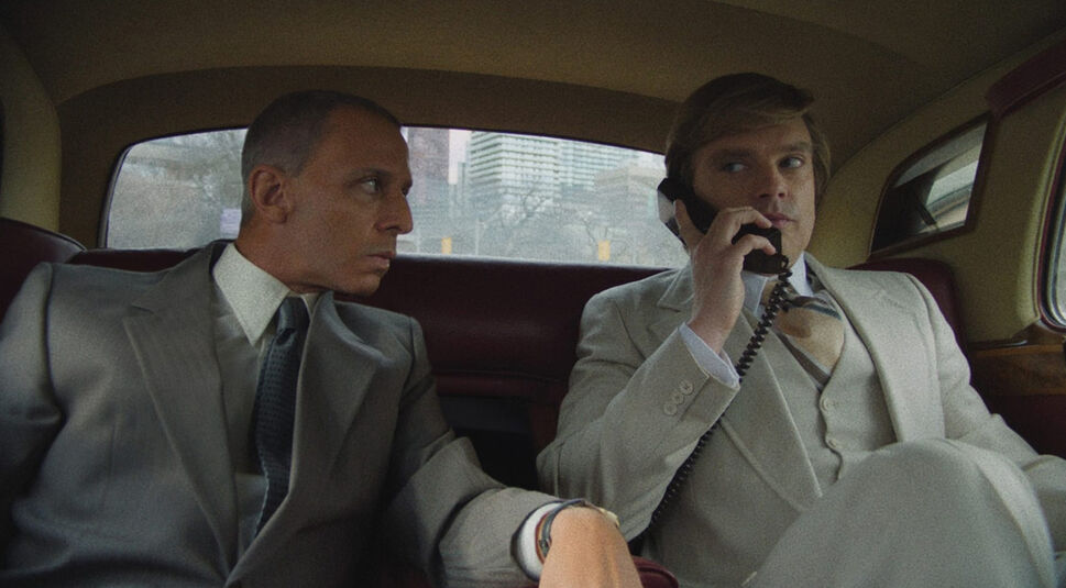 Auf dem Bild in dem Artikel zu den Oscar Filmen 2025, die bei GigaTV verfügbar sind, ist eine Szene aus The Apprentice zu sehen. Zwei Männer in eleganten Anzügen sitzen auf der Rückbank eines Autos mit ledernen Sitzen. Der Mann rechts, in einem hellen Anzug mit Krawatte, telefoniert mit einem kabelgebundenen Autotelefon und wirkt konzentriert. Der Mann links, in einem dunkleren Anzug, schaut ihn aufmerksam an. Durch das Fenster sind Hochhäuser und eine Stadtlandschaft zu erkennen. Die Szene vermittelt eine angespannt-geschäftliche Atmosphäre.