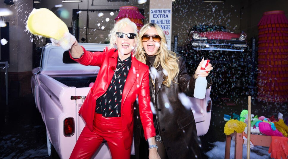 In dieser Szene aus GNTM 2025 Folge 13 sind Ellen von Unwerth in einem roten Lederanzug und Heidi Klum in einem langen, dunklen Mantel zu sehen. Beide lachen ausgelassen beim Autowaschen, mit Seifenblasen in der Luft und Requisiten im Hintergrund. Die Stimmung ist energiegeladen und verspielt, typisch für ein kreatives GNTM-Shooting.