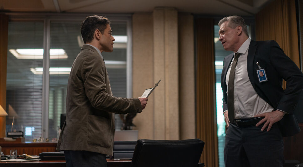 In dieser Szene aus The Amateur stehen sich Charles Heller, gespielt von Rami Malek, und Moore, dargestellt von Holt McCallany, in einem Büro gegenüber. Heller hält ein Dokument in der Hand und wirkt entschlossen, während Moore mit strengem Blick und Händen in der Hüfte konfrontativ wirkt. Die angespannte Stimmung deutet auf einen intensiven Moment im Geheimdienstmilieu hin.