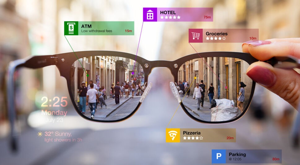Das Bild zum Thema Was ist Augmented Reality zeigt eine Stadtstraße durch eine Brille, in deren Gläser digitale Informationen eingeblendet sind. Über die reale Umgebung werden virtuelle Hinweise zu Hotels, Restaurants, Wetter und Parkplätzen angezeigt. Die Szene illustriert, wie Augmented Reality den Alltag durch zusätzliche Informationen in Echtzeit unterstützt.
