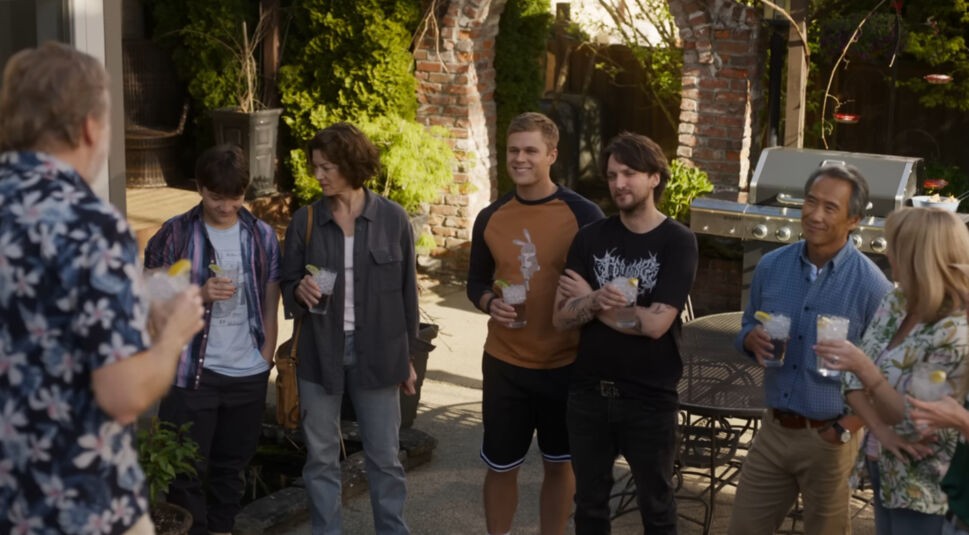 Freunde und Familie stehen gemeinsam im Garten, halten Getränke in den Händen und lächeln.