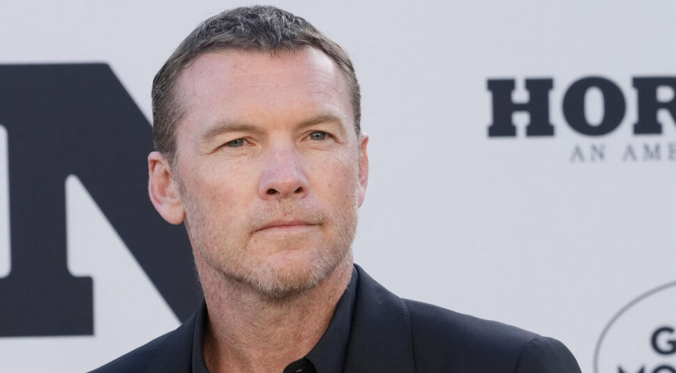 Auf dem Bild zur Nur für Dein Leben Netflix-Serie ist Sam Worthington in einem eleganten schwarzen Anzug vor einer neutralen Hintergrundwand mit großem Schriftzug zu sehen. Er blickt ruhig und ernst zur Seite, sein Gesichtsausdruck wirkt konzentriert und nachdenklich.