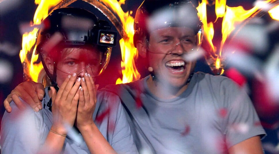 Auf dem Bild in dem Artikel zu den Sommerhaus der Stars-Gewinner:innen sind Antonia Hemmer und Patrick Romer aus Staffel 7 in einem emotionalen Moment zu sehen. Beide tragen Helme und Schutzbrillen. Patrick lacht ausgelassen, während Antonia sich scheinbar überwältigt die Hände vor das Gesicht hält.