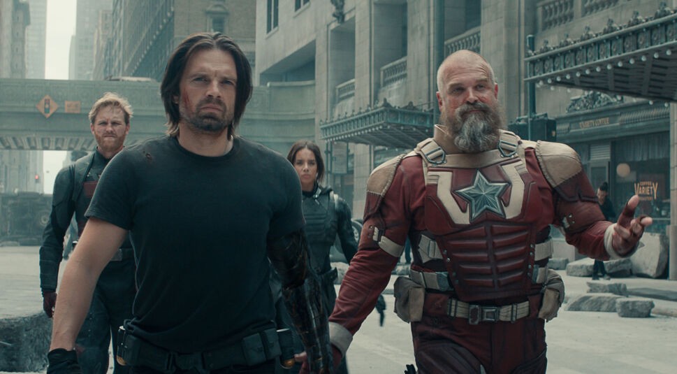 Auf dem Bild zur Thunderbolts* Kritik marschieren John Walker (Wyatt Russell), Bucky Barnes (Sebastian Stan), Ghost (Hannah John-Kamen) und Red Guardian (David Harbour) entschlossen durch eine zerstörte Stadt. Im Vordergrund sieht man Bucky mit grimmigem Blick und Red Guardian in rot-weißer Rüstung, der mit einer Geste spricht. Die Szene wirkt angespannt, dynamisch und zeigt das Team in Aktion.