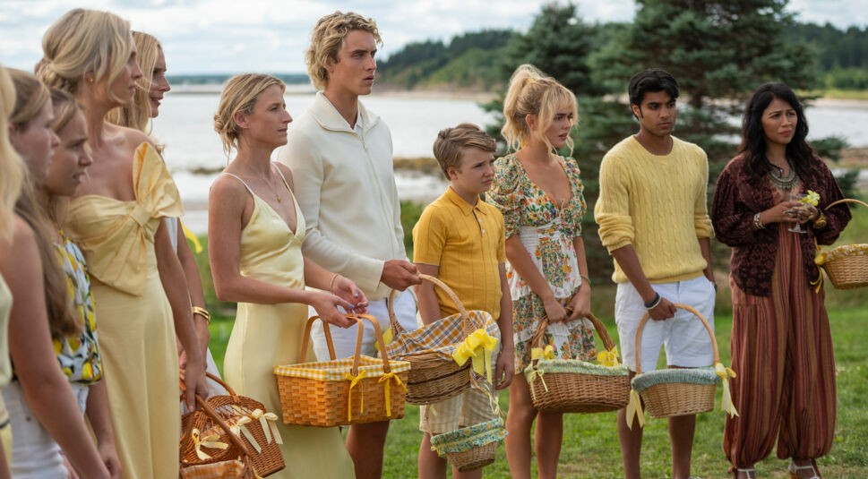 Auf dem Bild zur We Were Liars-Serie ist eine Gruppe von Menschen scheinbar bei einem sommerlichen Picknick zu sehen. Die meisten tragen festliche Kleidung in Gelb- und Cremetönen und halten Picknickkörbe in den Händen. Die Szene spielt im Grünen. 