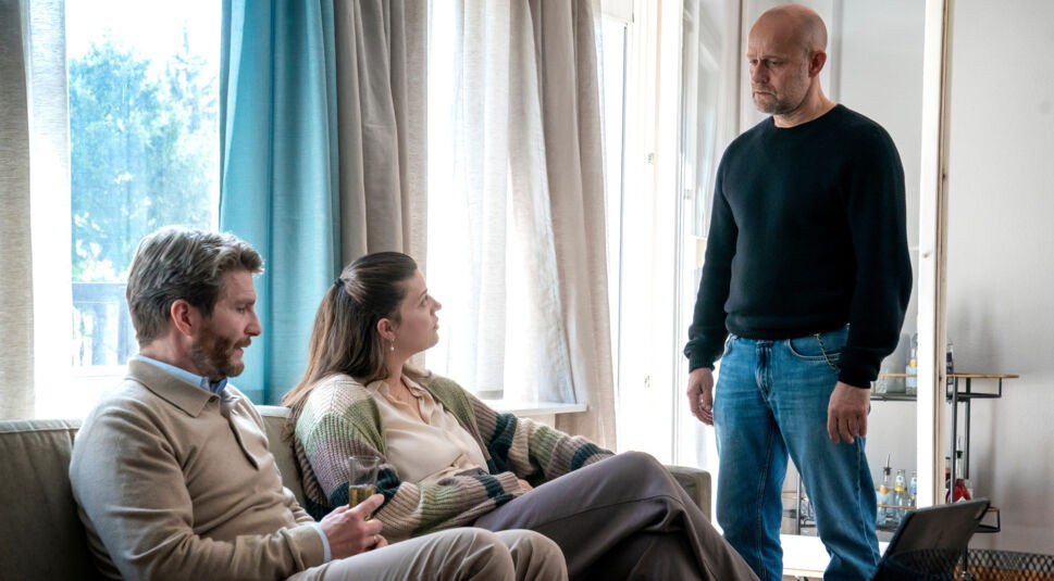 Zwei Personen sitzen auf einem Sofa, eine Person steht vor ihnen.