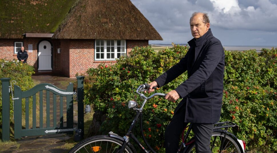 Schauspieler Peter Heinrich Brix kommt mit einem Fahrrad an einem Haus auf Sylt an.