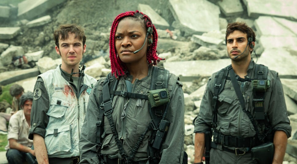 In der Alien: Earth Serie stehen Hermit, Siberian und Rashidi – gespielt von Alex Lawther, Diêm Camille und Moe Bar-El – inmitten einer zerstörten Betonlandschaft. Alle drei tragen taktische Kampfanzüge mit Headsets und schauen konzentriert in unterschiedliche Richtungen. 