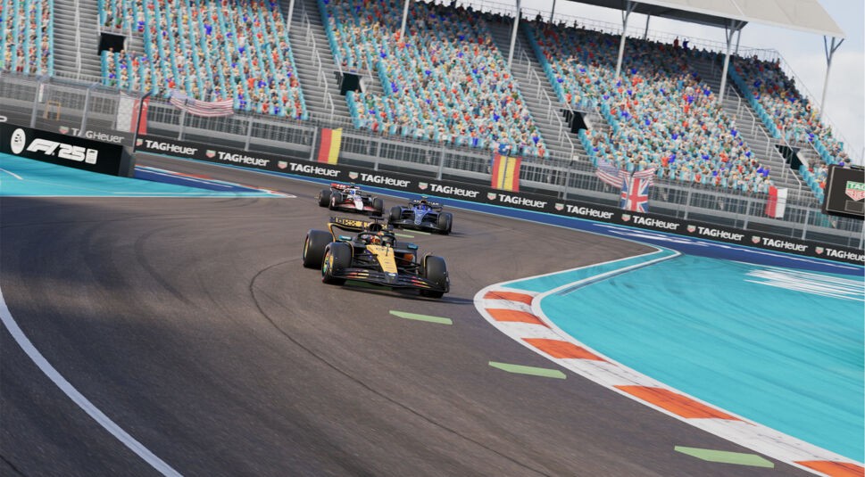 Im Bild zum F1 25 Test liefern sich drei Formel-1-Boliden auf einer modernen Stadtrennstrecke ein Kopf-an-Kopf-Rennen. Der führende Wagen fährt durch eine Kurve mit auffälligem blau-orangefarbenem Randbereich. Die Tribünen im Hintergrund sind voll besetzt, während Banner von TAG Heuer und Länderflaggen die Atmosphäre verstärken.