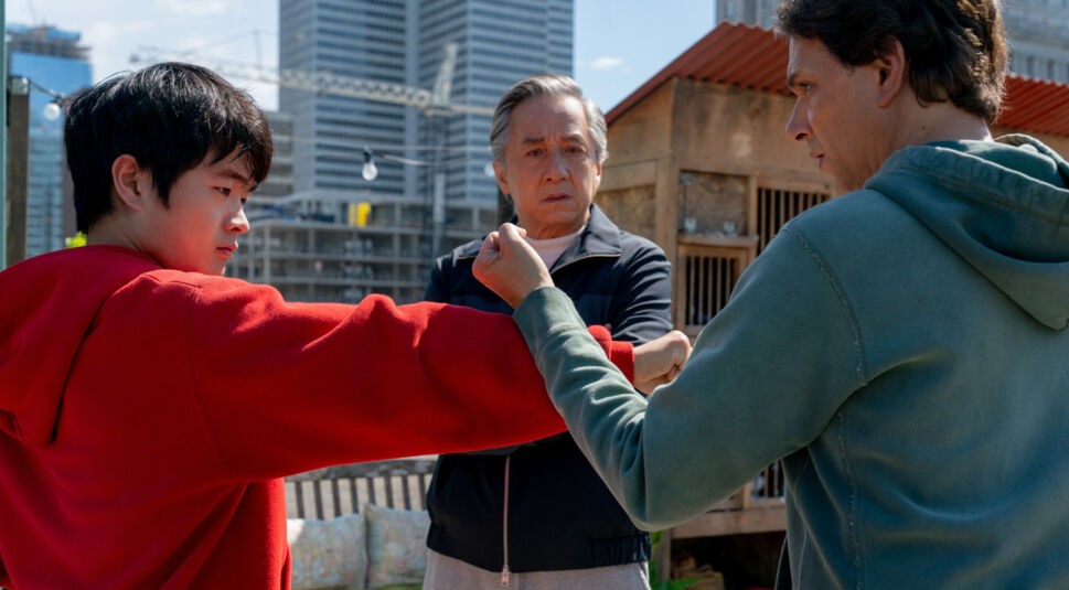 In dieser Szene aus Karate Kid: Legends stehen sich Ben Wang als Li Fong und Ralph Macchio in einer Trainingshaltung gegenüber, während Jackie Chan konzentriert zwischen ihnen steht. Alle drei tragen Freizeitkleidung. Die Szene wirkt intensiv und lehrreich – ein zentrales Motiv für die Karate Kid: Legends Kritik.