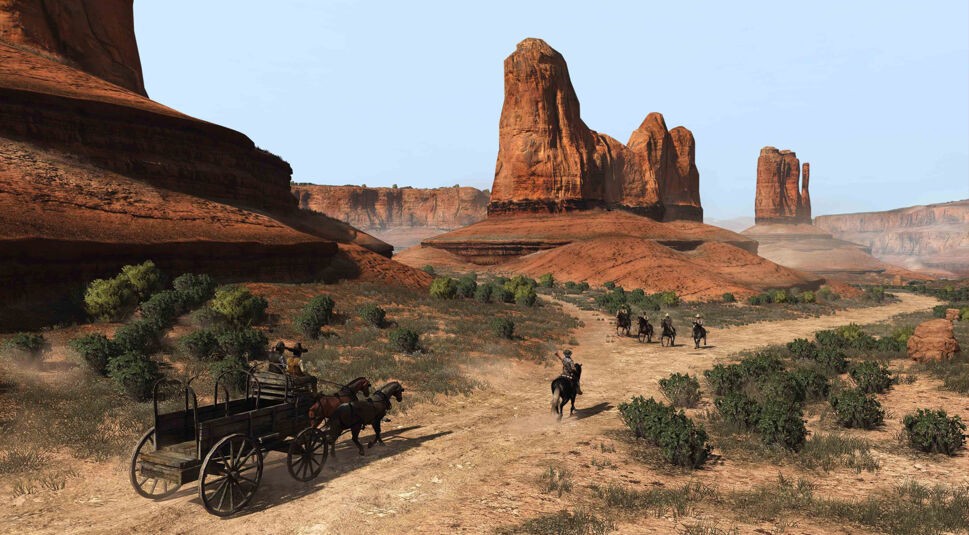 Im Screenshot aus Red Dead Redemption durchquert eine Reitergruppe mit Planwagen eine karge Wüstenlandschaft mit gewaltigen Felsformationen im Hintergrund. Die Szene erinnert stark an klassische Westernfilme und könnte ein verstecktes Red Dead Redemption Easter Egg darstellen, das sich auf ikonische Orte des Genres bezieht.
