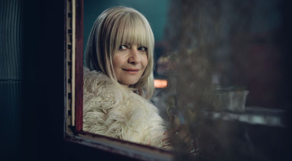 Małgorzata Kożuchowska in Aniela: Eine blonde Frau mit weißem Pelzmantel betrachtet sich lächelnd in einem Spiegel.