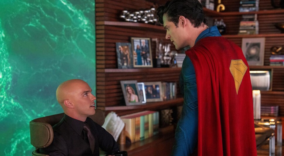 Nicholas Hoult und David Corenswet in Superman: in Mann mit Glatze sitzt auf einem Ledersessel, hält eine Kaffetasse in der Hand und blick hoch zu dem vor ihm stehenden Superman.