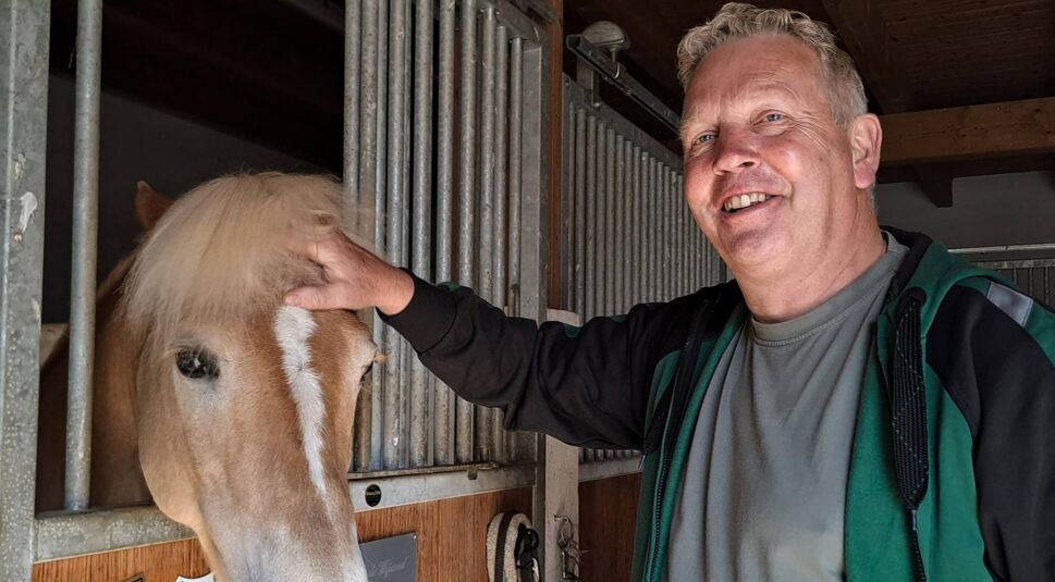 Bei Bauer sucht Frau 2025 streichelt Kandidat Jörg lächelnd ein Haflinger-Pferd im Stall. In grauem Shirt und Jacke wirkt er freundlich und tierlieb in der ruhigen Stallumgebung.