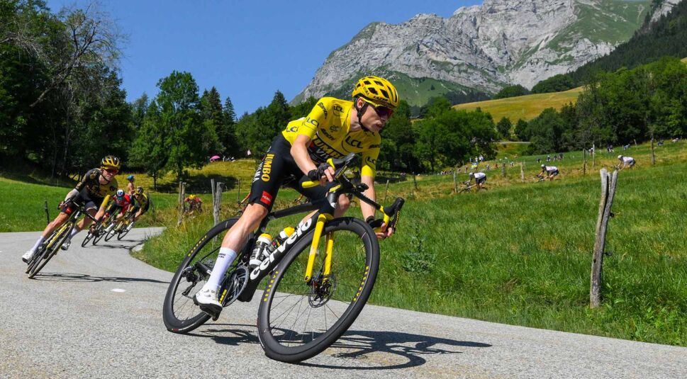 In den GigaTV-Highlights im Juli 2025 siehst du ein Bild von der Tour de France 2023: Ein Radfahrer im gelben Trikot des Gesamtführenden fährt mit hoher Geschwindigkeit durch eine Kurve in alpiner Landschaft.
