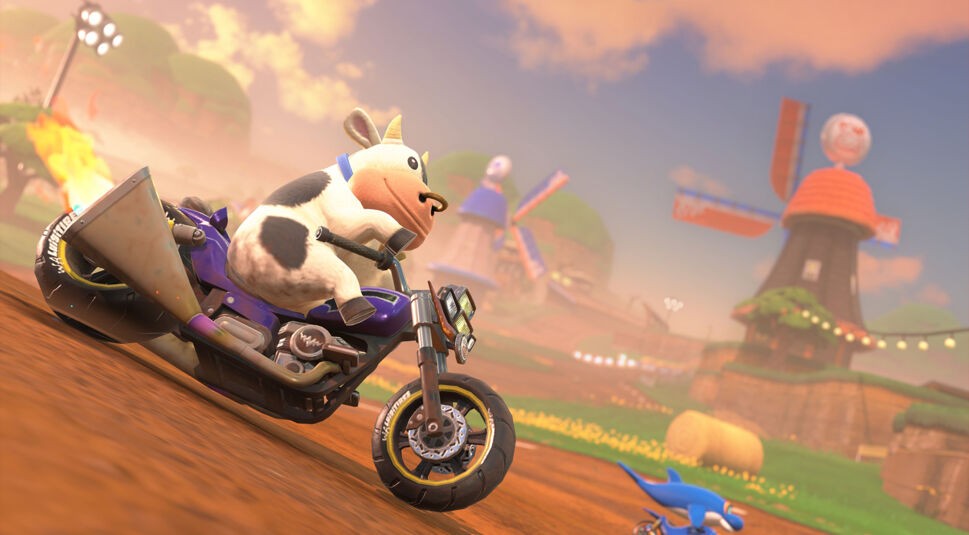 Auf dem Bild in dem Artikel zum Mario Kart World-Test ist eine Szene aus dem Videospiel zu sehen. Eine Kuh rast auf einem Motorrad bei Sonnenuntergang über eine Farm-Rennstrecke. Im Hintergrund stehen Windmühlen und Strohballen.