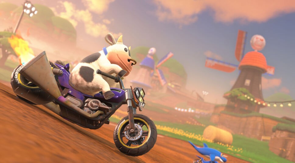 Im Bild zu Mario Kart World Tipps fährt eine schwarz-weiße Kuh als spielbarer Charakter auf einem violetten Motorrad durch eine ländliche Strecke mit Windmühlen, Feldern und Strohballen. Der Himmel ist in warmes Licht getaucht und vermittelt eine verspielte, fast absurde Atmosphäre – typisch für die kreativen Kurse von Mario Kart.