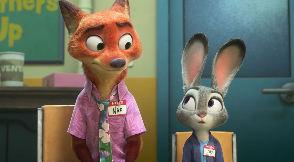 Auf dem Bild zu Zoomania 2 sitzen Nick Wilde und Judy Hopps auf Stühlen. Nick, ein rot-orangefarbener Fuchs im Hawaiihemd, schaut verlegen zur Seite, während Judy, eine graue Häsin in Uniform, ihn überrascht ansieht. Beide tragen Namensschilder.