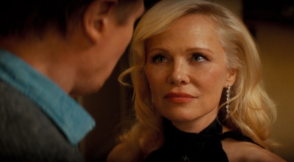 Pamela Anderson ist in ihrer Rolle als Beth in einer Nahaufnahme aus dem neuen Die nackte Kanone Film zu sehen. Ihr Blick ist ruhig, aber durchdringend, während sie einer männlichen Figur gegenübersteht. Mit eleganten Ohrringen, roten Lippen und einem schwarzen Kleid verkörpert sie Glamour und Geheimnis – passend zum humorvollen Ton von Die nackte Kanone.        ChatGPT fragen