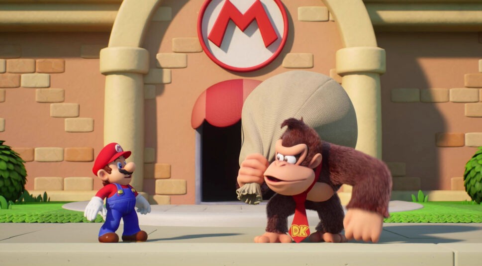 In dieser Szene aus einem der Donkey Kong-Spiele stehen sich Donkey Kong und Mario vor dem Eingang zu einem Gebäude mit rotem M-Logo gegenüber. Donkey Kong trägt einen Sack über der Schulter, während Mario überrascht schaut.