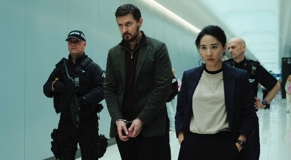 In den GigaTV-Highlights im August ist eine Szene mit Dr. Matthew Nolan, gespielt von Richard Armitage, und einer Polizistin, dargestellt von Jing Lusi, zu sehen. Nolan wird mit Handschellen von bewaffneten Beamten abgeführt, während Lusi ernst und entschlossen voranschreitet.