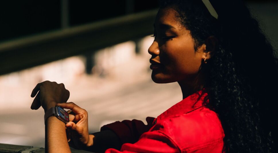 Frau mit rotem Hemd schaut auf ihre Apple Watch 11 am Handgelenk.