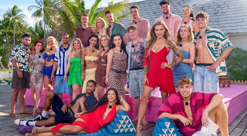 Auf dem Gruppenbild zu Are You The One Realitystars in Love Staffel 5 posieren die Teilnehmer:innen auf einer sonnigen Terrasse. In farbenfroher, sommerlicher Kleidung stehen sie nebeneinander und lächeln in die Kamera.