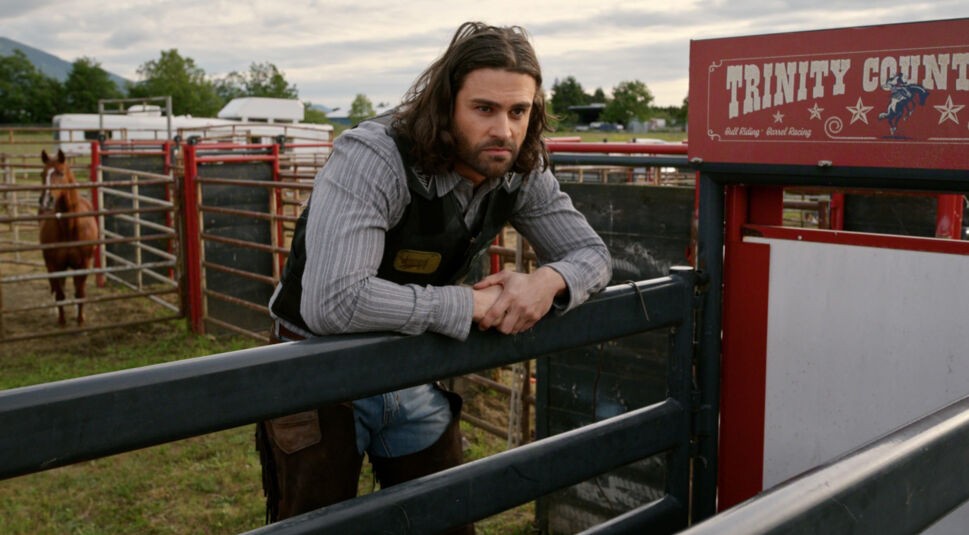 Clay (Cody Kearsley) steht in einem Pferdegehege und stützt sich mit beiden Armen auf das Geländer.