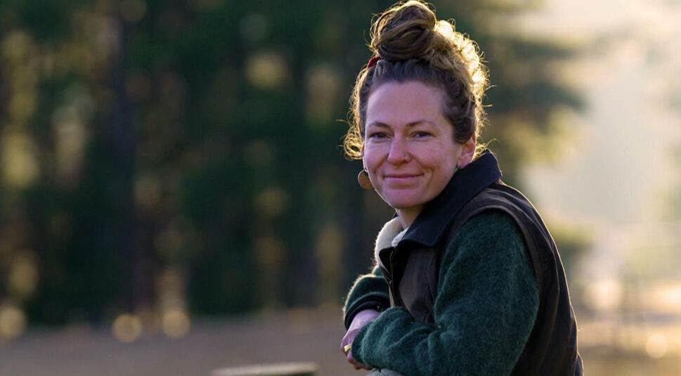 Auf dem Bild zu Bauer sucht Frau International 2026 steht eine Frau mit Dutt lächelnd an einem Zaun.