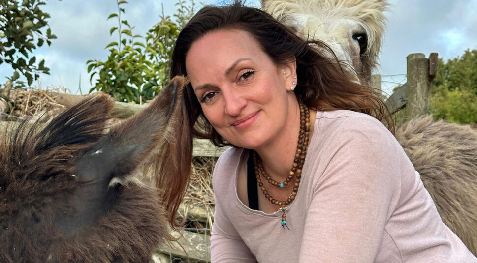 Auf dem Bild zu Bauer sucht Frau International 2026 ist eine Frau und zwei Tiere zu sehen. Sie trägt eine lange Kette und ein helles Oberteil.