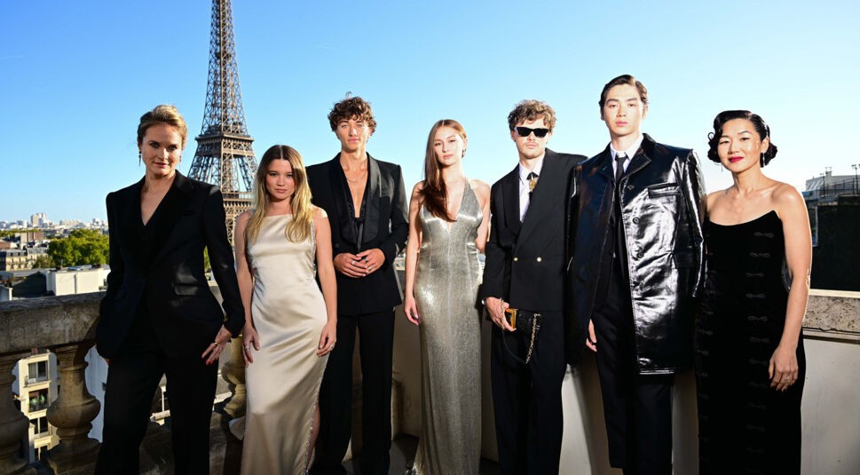 Auf dem Bild in dem Artikel zum Der Sommer, als ich schön wurde-Film ist der Hauptcast der Serie vor dem Eiffelturm in Paris zu sehen. Alle Darsteller:innen tragen elegante Abendgarderobe – von glänzenden Kleidern bis hin zu modernen Anzügen. Die Gruppe steht auf einer Dachterrasse bei Sonnenschein.