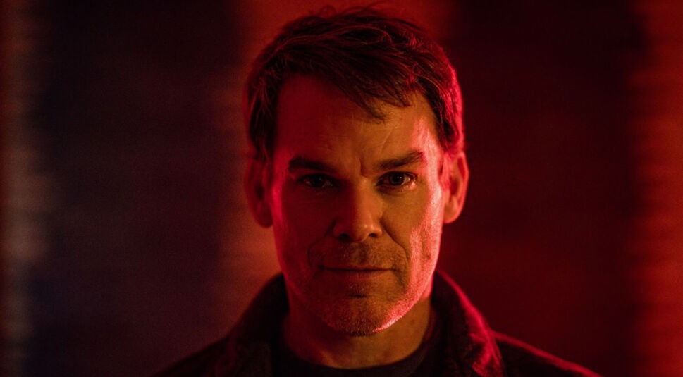 Auf dem Bild zur Serie Dexter Wiedererwachen ist Dexter Morgan zu sehen, gespielt von Michael C. Hall. Er steht im Mittelpunkt des Bildes, sein Gesicht wird von dramatischem, rötlichem Licht betont, was eine düstere und intensive Stimmung erzeugt. Die Szene wirkt geheimnisvoll und emotional aufgeladen