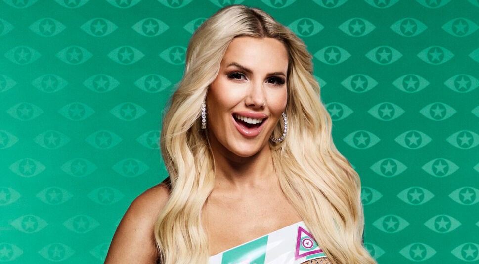 Eine Kandidatin von Promi Big Brother 2025 mit langen, offenen, blonden Haaren und auffälligem Glitzerkleid ist in das Klebeband mit dem Slogan „Die Fassade fällt“ eingewickelt und lächelt in die Kamera.