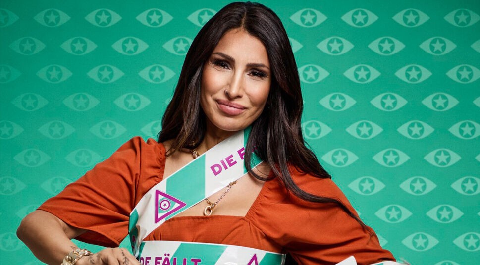 Pinar Sevim trägt auf dem Promi Big Brother 2025 Bild ein rotes Kleid. Ihr Oberkörper ist mit den typischen Bändern umwickelt, auf denen der Slogan „Die Fassade fällt“ zu lesen ist.
