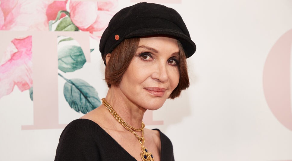 Auf dem Bild in dem Artikel zu Promis unter Palmen 2026 ist Anouschka Renzi in einem schwarzen Oberteil und mit goldener Kette zu sehen. Sie trägt eine schwarze Mütze und blickt in die Kamera.