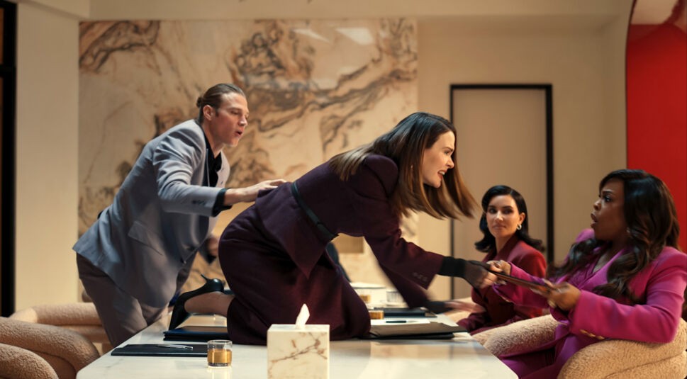 In dieser dramatischen Szene aus All's Fair kniet Sarah Paulson als Carr Lane wütend auf einem Konferenztisch und streitet mit Niecy Nash-Betts als Emerald Greene, die erschrocken zurückweicht. Links versucht Alluras Exmann, die Situation zu beruhigen, während Kim Kardashian als Allura Grant das Geschehen angespannt beobachtet. Die Stimmung ist explosiv und voller Spannung.