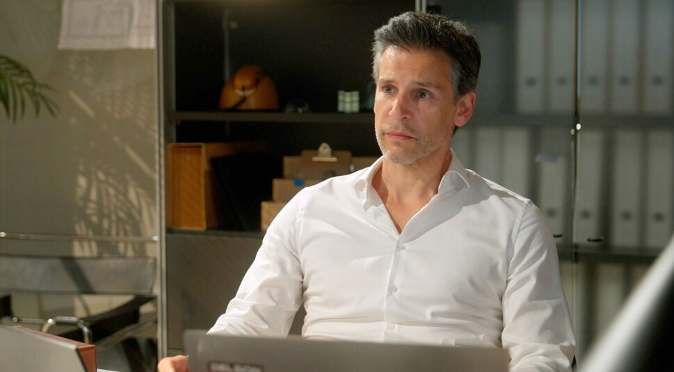 Im Bild zur Besetzung von Rote Rosen in Staffel 24 ist Richard, gespielt von Florian Odendahl, in einem modernen Büro zu sehen. Er trägt ein weißes Hemd und sitzt nachdenklich vor seinem Laptop. Die Szene wirkt ruhig und konzentriert, mit Aktenordnern und Regalen im Hintergrund, was auf ein berufliches Umfeld hinweist.