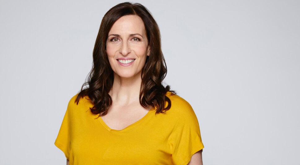 Auf diesem Bild zur GZSZ-Besetzung ist Ulrike Frank zu sehen. Sie trägt ein gelbes Oberteil und lächelt in die Kamera.