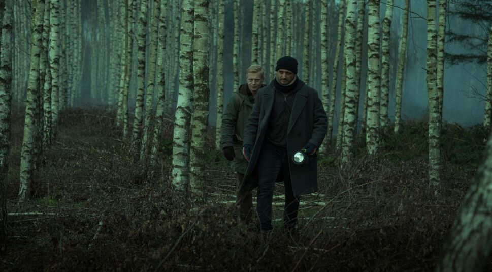 Auf dem Bild zu den internationalen Sendern und TV-Paketen bei Vodafone ist eine düstere Szene aus der polnischen Crime-Serie „Kruk“ zu sehen. Zwei Männer gehen durch einen nebligen Birkenwald, einer hält eine Taschenlampe in der Hand.