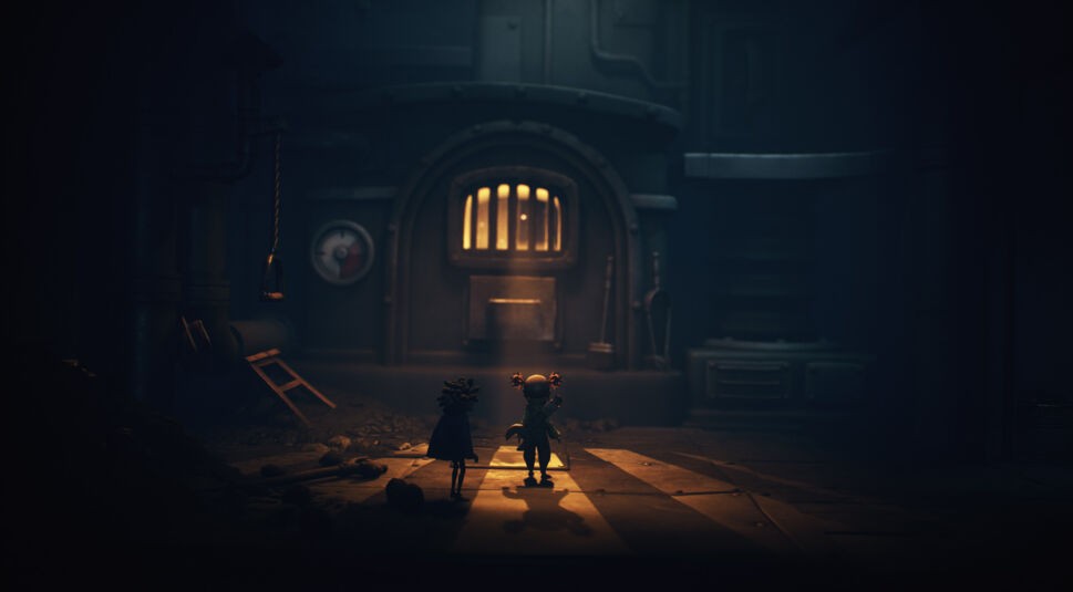 Auf dem Bild im Little Nightmares 3-Tipps-Artikel stehen die beiden Charaktere Low und Alone nebeneinander vor einer großen, beleuchteten Metalltür. Die Umgebung ist düster und industriell geprägt, mit Rohren, Schatten und warmem Licht, das durch das Gitterfenster fällt.