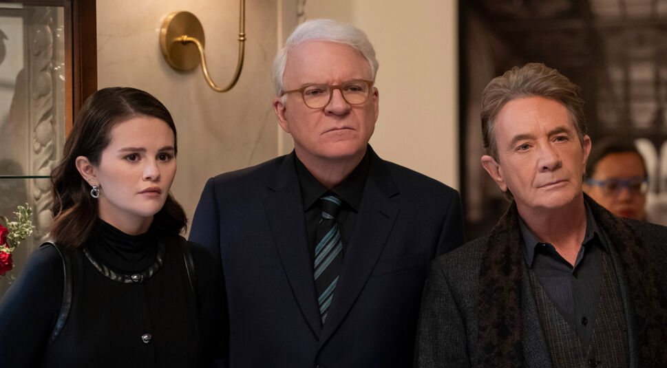 Auf dem Bild in dem Artikel zu Only Murders in the Building Staffel 6 blicken Charles, Oliver und Mabel ernst in eine Richtung. Charles trägt einen dunklen Anzug, Oliver ein graues Jackett mit Schal, Mabel ist in einem schwarzen Outfit mit Ohrringen zu sehen.